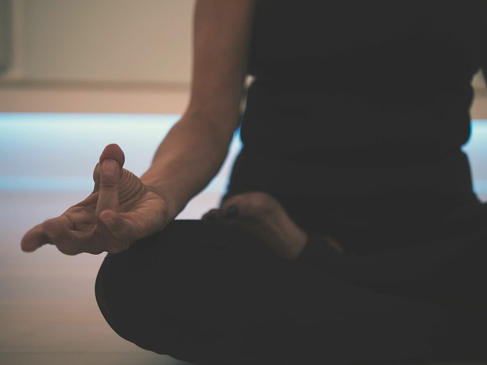Frau im Schneidersitz mit yoga-typischer Handhaltung.