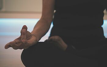 Frau im Schneidersitz mit yoga-typischer Handhaltung.