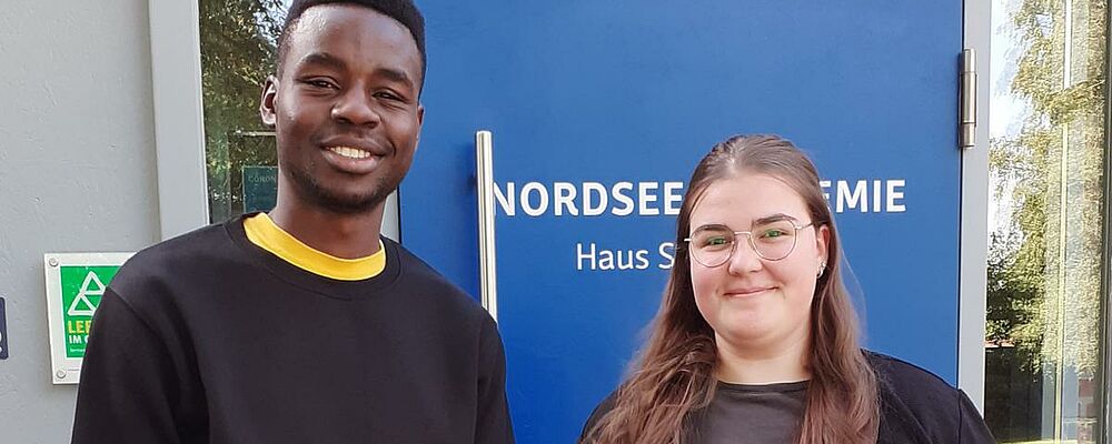 Eine junge Frau und ein junger Mann stehen vor dem Eingang der Nordsee Akademie.