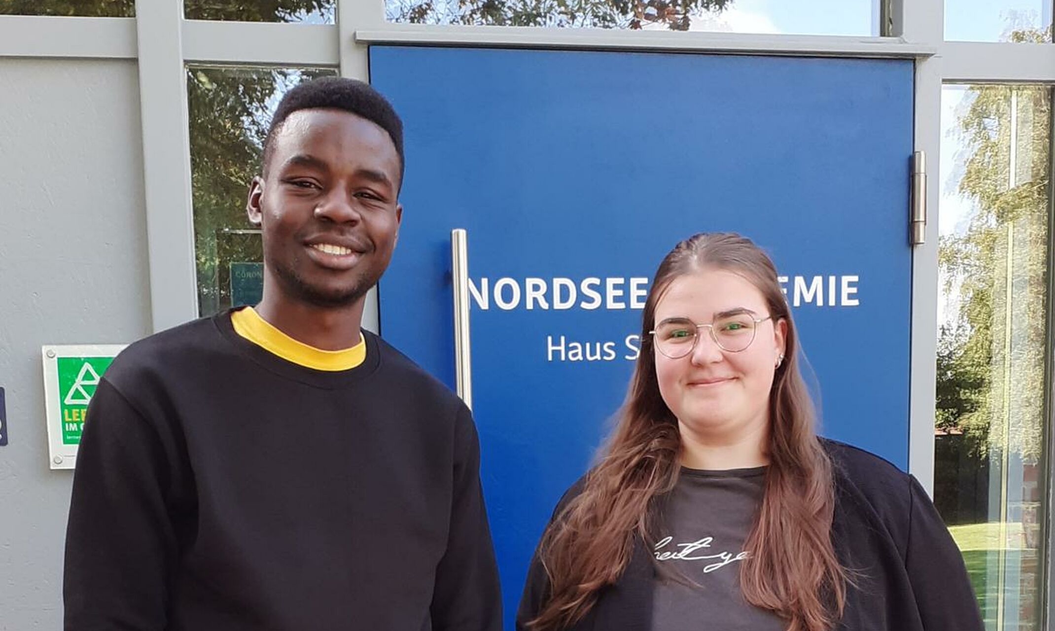 Eine junge Frau und ein junger Mann stehen vor dem Eingang der Nordsee Akademie.