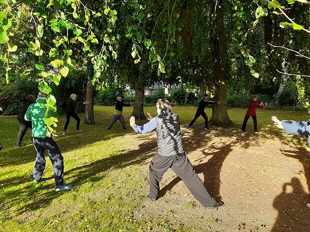 Eine Gruppe Erwachsener macht Qi-Gong-Übungen in einem Waldstück