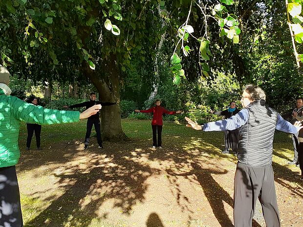 Eine Gruppe Erwachsener macht Qi-Gong-Übungen in einem Waldstück.