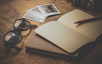 Brille, aufgeschlagenes Heft, Stift und alte Fotos auf einem Tisch