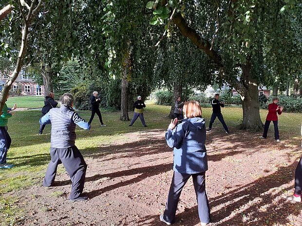 Eine Gruppe Erwachsener macht Qi-Gong-Übungen in einem Waldstück.